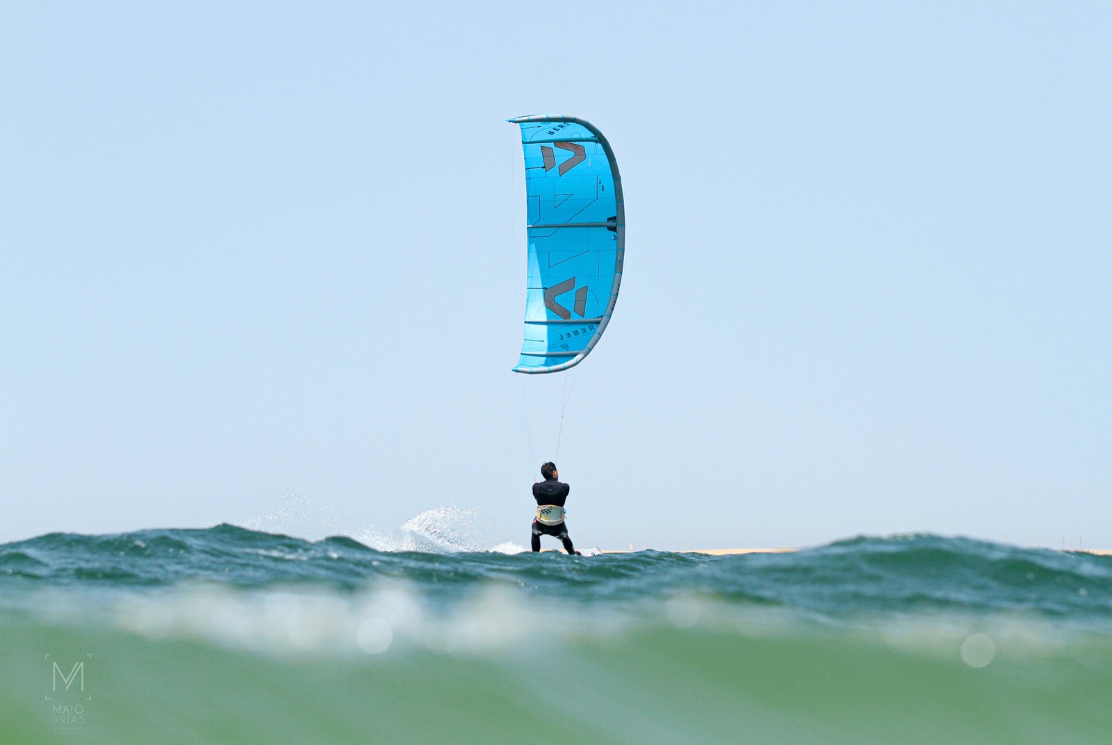Kitesurfista navegando entre olas con una cometa azul, visto desde la superficie del agua.