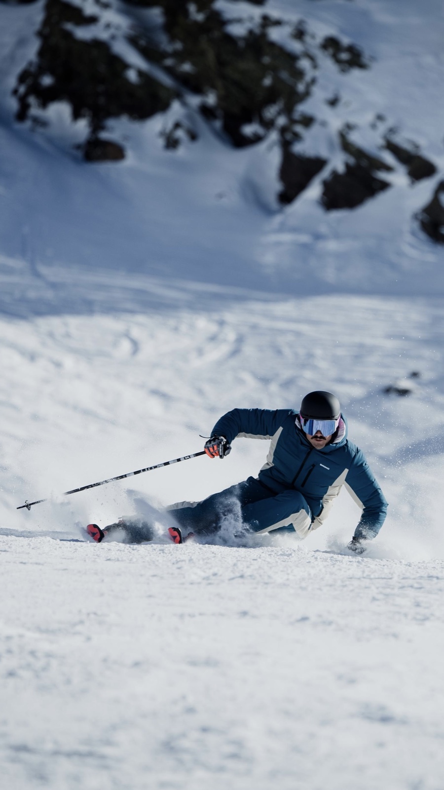 Esquiador con ropa azul trazando un giro en la nieve junto a unas rocas.