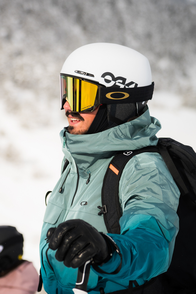 Retrato de perfil de un esquiador con casco blanco, máscara amarilla y chaqueta azul en la nieve.